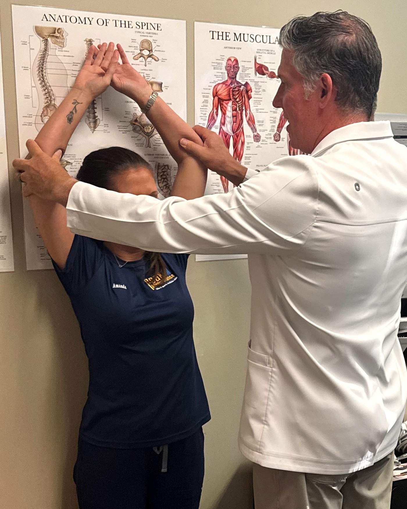 Indicator 3, the wall test: a patient stands with her back to the wall, arms raised overhead, while the chiropractor guides her arms to read how far they fall short of flat